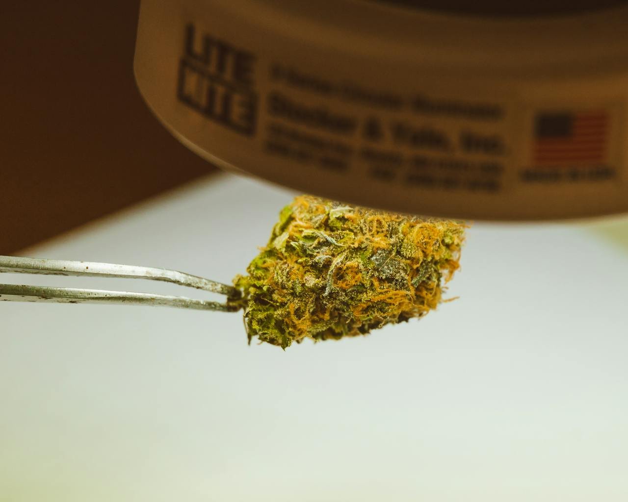 who-we-are Detailed view of a cannabis bud held by tweezers under a light, emphasizing texture and trichomes.